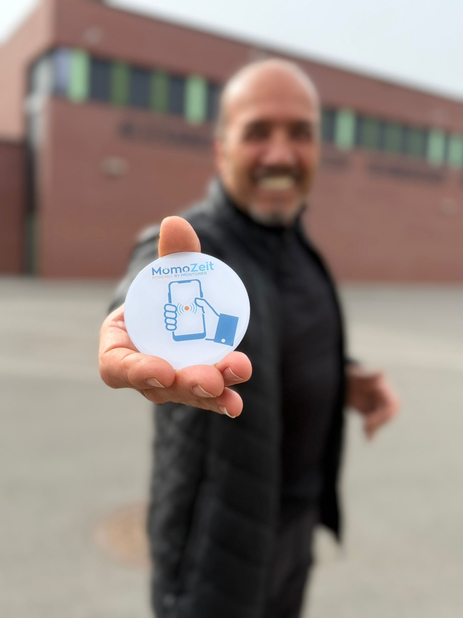 Mann hält MomoZeit NFC-Sticker in die Kamera